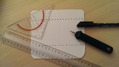 Ein Geodreieck und Lineale liegen auf einem Blatt Papier, während eine Schneidelineal und ein Stift bereit für Präzisionsarbeit sind.