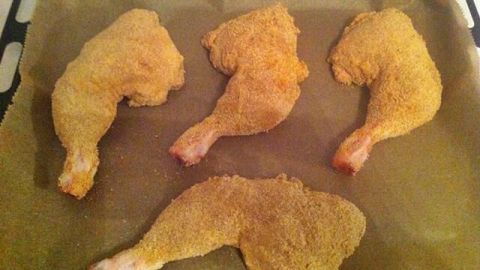 Panierte Hühnerschenkel ohne Haut liegen auf einem Backblech, bereit zum Garen, goldbraun und knusprig.
