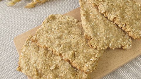 Hafer-Knäckebrot liegt auf einem Holzbrett, umgeben von Haferähren, bereit zum Genießen in einer hellen Umgebung.