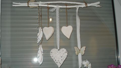 Eine h&auml;ngende Deko aus Zweigen mit wei&szlig;en Herzen und Federn schm&uuml;ckt ein Fenster im shabby chic Stil.