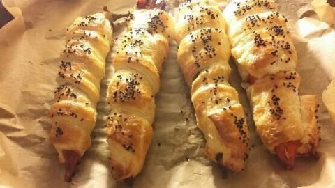 Gefüllte Paprika mit Schafskäse sind in goldbraunem Blätterteig gebacken, auf Backpapier in einer warmen Umgebung platziert.