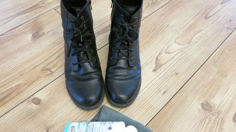 Alternative für teure Schuhcreme: Schuhe ganz einfach mit Hand- oder Gesichtscreme zum Glänzen bringen. Schwarze Stiefel stehen auf einem Holzboden, während Handcreme neben ihnen liegt, bereit zum Glänzenbringen der Schuhe.