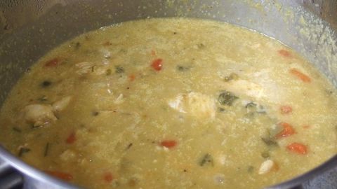 Ein Topf mit Hähnchen-Restverwertung kocht eine dicke, grüne Suppe mit Gemüse und Stückchen von Hähnchen.