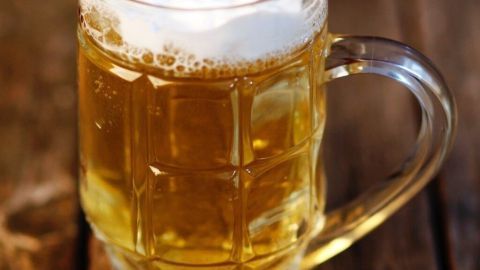 Ein gefülltes Bierglas steht auf einer rustikalen Holztischplatte, die einladend aussieht und zur Geselligkeit einlädt.