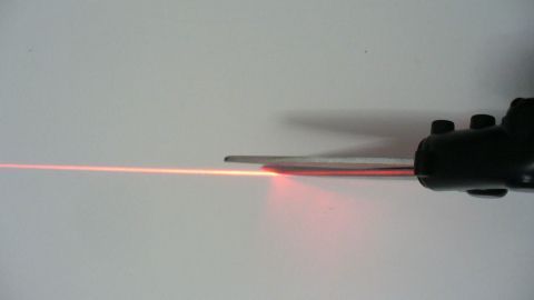 Eine Schneiderschere mit Laserschnittführung schneidet präzise durch Stoffe, unterstützt von einem roten Laserstrahl.