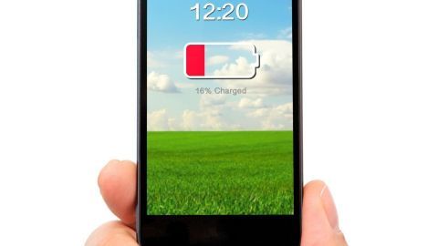 Ein Smartphone zeigt 10 % Akkustatus auf dem Bildschirm, während eine Hand es hält. Im Hintergrund sind grüne Wiesen und ein blauer Himmel.