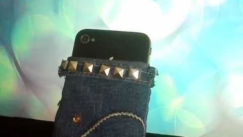 Eine Handytasche aus Jeans steht auf einem Tisch, während ein Smartphone darin steckt, vor einem verschwommenen, bunten Hintergrund.