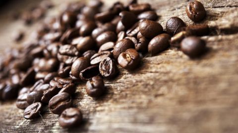 Röstende Kaffeebohnen liegen verstreut auf einer Holzoberfläche, die die gemütliche Atmosphäre eines Cafés vermittelt.