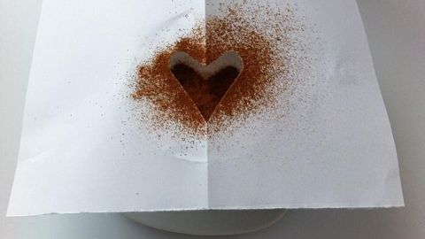 Eine Schablone liegt auf einem Dessert, während Kakaopulver in Form eines Herzens darüber gestreut wird.