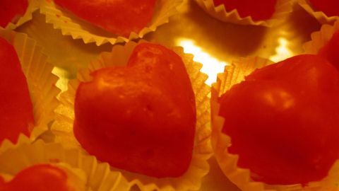 Rote Herzgebäcke liegen in kleinen Förmchen auf einem goldenen Untergrund und verleihen einen liebevollen Eindruck.