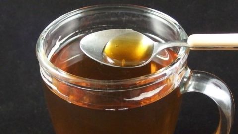 Ein Glas Tee, aus dem ein Löffel gefüllt wird; ideal für kleine Schlücke gegen Halsschmerzen in einem dunklen Umfeld.