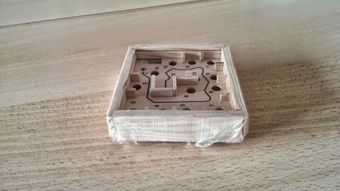 Ein Spiel mit einer kugelartigen Form in einem Holzrahmen, das durch ein Labyrinth geführt wird, liegt auf einem Tisch.