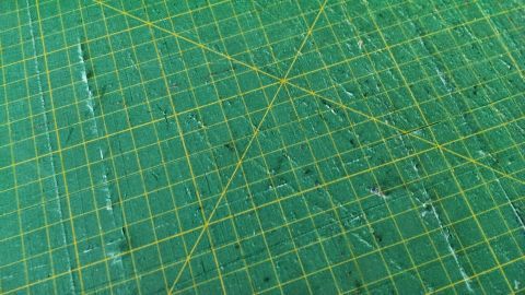 Eine stark benutzte Schneidematte liegt auf einem Tisch und zeigt Abnutzungsspuren, die für eine Reinigung vorbereitet wird.
