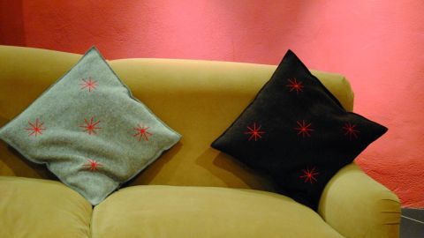 Ein gelbes Sofa mit zwei Kissen, einem grünen und einem schwarzen, steht vor einer rot gestrichenen Wand.