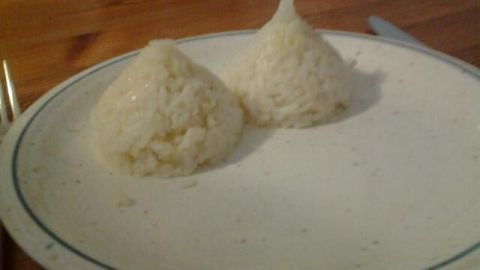 Zwei Reishütchen, die auf einem weißen Teller serviert werden, liegen vor einem schlichten Holztisch.