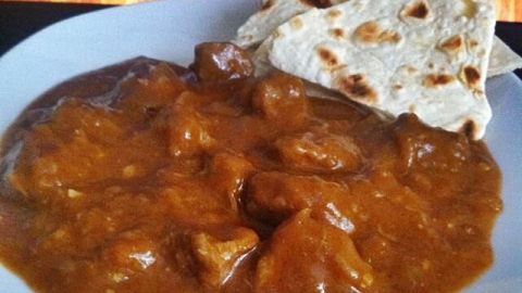 Ein Teller Gulasch ist mit einer dicken, würzigen Sauce gefüllt, während daneben ein Stück Brot liegt; der Hintergrund zeigt ansteigende Flammen.