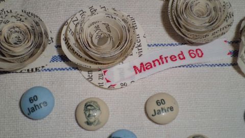 Schlichte Tischdeko mit Papierrosen und Buttons, die für den Geburtstag von Manfred mit "60 Jahre" dekoriert sind.