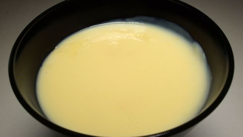 Ein schwarzes Schüsselchen hält cremigen Tütenpudding, der glatte, geleeartige Konsistenz zeigt, vor neutralem Hintergrund.