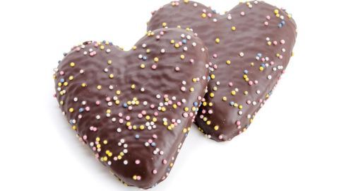 Zwei herzförmige Schokoladenplätzchen mit bunten Streuseln liegen zusammen auf einem weißen Untergrund, bereit zum Genießen.