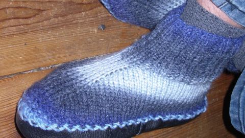 Ein paar gestrickte Socken mit einem farbverlauf in Blau und Grau liegen auf einem Holzboden, umgeben von Jeans.