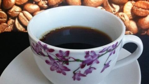 Eine Kaffeetasse mit schwarzem Kaffee steht auf einem herzförmigen Unterteller, vor einem Hintergrund aus Kaffeebohnen.