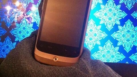Ein Sitzsack aus Jeansstoff hält ein Smartphone stabil. Der Hintergrund zeigt ein farbenfrohes, festliches Muster.