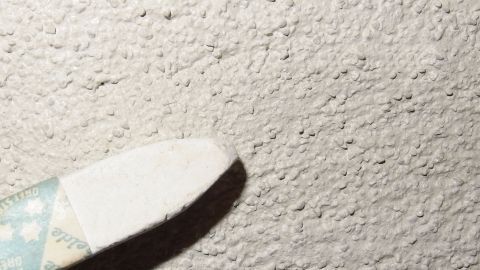 Leichte Beschädigungen oder Schmutzflecken auf weißer Zimmerwand- oder Decke an der Raufaser kaschieren. Eine Hand mit einem Reinigungswerkzeug entfernt Schmutzflecken von einer weißen, strukturierten Zimmerwand.