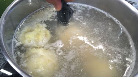 Kartoffelknödel schwimmen in sprudelndem Wasser, während jemand mit einer Küchenhilfe sie vorsichtig wendet.
