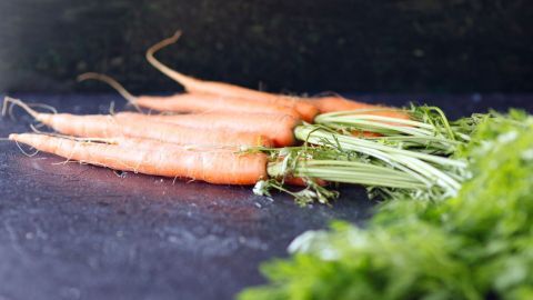 Frische Möhren liegen auf einer dunklen Oberfläche, während das Grünzeug daneben ausgebreitet ist, ideal für Möhrensirup.