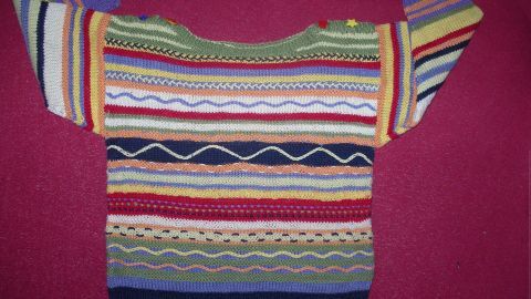 Ein bunten Pullover mit Jacquardmustern liegt auf einem roten Untergrund, er zeigt verschiedene Streifen und Wellenmuster.