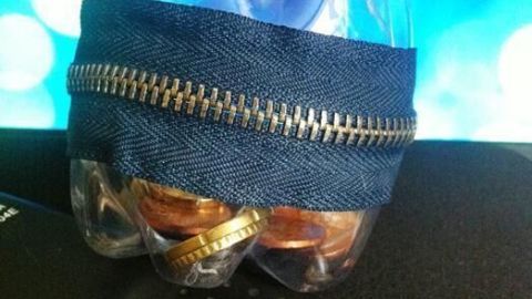 Ein wiederverwendeter Behälter aus einer Plastikflasche, umhüllt von Jeansstoff, steht auf einem dunklen Tisch.