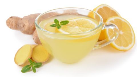 Eine Tasse heißes Wasser mit Ingwer und Zitrone steht auf einem weißen Tisch, umgeben von Ingwerwürfeln und Zitronenscheiben.