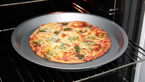 Eine frisch zubereitete Tiefkühlpizza liegt auf einem Backblech im Ofen und wird goldbraun gebacken.