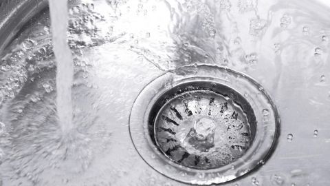 Ein Abfluss im Waschbecken wird von strömendem Wasser gespült, während er eine glatte, glänzende Oberfläche zeigt.