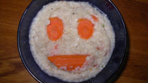 Eine Schüssel Haferflocken mit einem lächelnden Gesicht aus Karottenstücken zeigt ein freundliches, einladendes Gericht, passend als Schonkost bei Durchfall.
