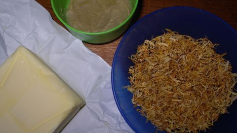 Eine gelbe Butterblock liegt neben einer Schüssel mit Kräutermischung und einer weiteren Schüssel mit einer Paste.