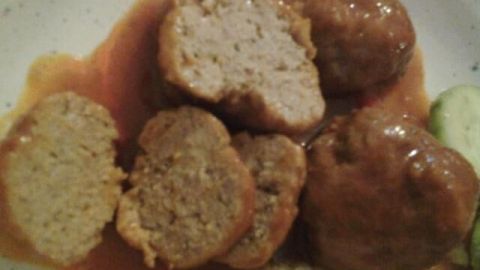 Saftige Albóndigas liegen auf einem Teller, umgeben von einer Tomatensauce und frischem Gemüse in einem gemütlichen Essbereich.