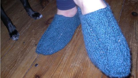 Stricksocken liegen in einer Holzumgebung, während Füße in selbstgemachten Sneakersocken eine entspannte Pose einnehmen.