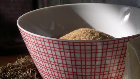 Eine Schüssel mit trockenem Thymian steht im Vordergrund, während aromatische Gewürze in einer Küche sorgsam arrangiert sind.