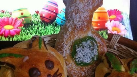 Hefeteig-Hasen liegen in einem Korb, während bunte Ostereier und Frühlingsblumen im Hintergrund zu sehen sind.