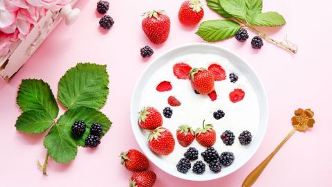 Eine Schüssel mit Buttermilchdessert ist mit frischen Erdbeeren und Brombeeren verziert, auf einem rosa Untergrund.
