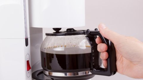 Eine Kaffeemaschine mit digitaler Zeitschaltuhr brüht frisch gebrauten Kaffee, während eine Hand die Kanne hält.