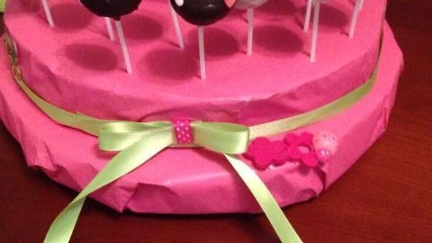 Ein pinker Cake Pop Halter zeigt eine Vielzahl köstlicher Cake Pops, die schön dekoriert und auf einem Tisch präsentiert sind.