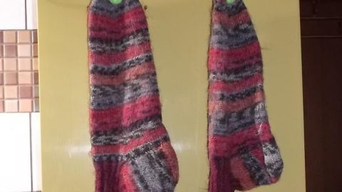 Bunte Stricksocken hängen an einem Kleiderbügel in einer hellen Umgebung und trocknen nach dem Waschen.