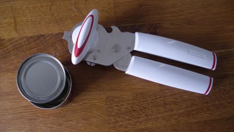 Ein Dosenöffner liegt auf einem Holztisch, neben einer geöffneten Dose, bereit zum sicheren Öffnen und Schließen.