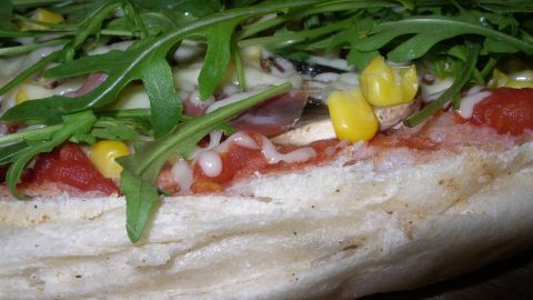 Eine frisch belegte Pizza mit bunten Zutaten wie Rucola und Mais liegt auf einem Holzbrett, bereit zum Genießen.