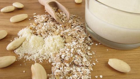 Haferflocken und Mandeln sind auf einem Holzbrett verstreut, während ein Glas mit milchiger Flüssigkeit daneben steht.