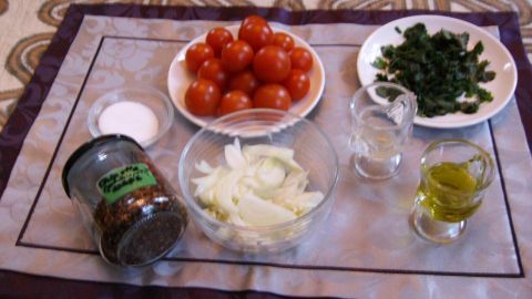 Runde Tomaten liegen auf einem Tisch, umgeben von Zutaten wie Zwiebeln, Kräutern, Öl und Gewürzen für Ensalada Chilena.