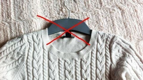 Ein gestrickter Pullover hängt an einem Kleiderbügel, der mit rotem Klebeband markiert ist, auf einem hellen Hintergrund.