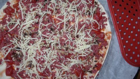 Eine Pizza liegt auf einem Backblech, belegt mit geriebener scharfer Knoblauchsalami (SUCUK) und K&auml;se.